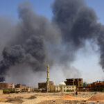 Man walks while smoke rises above buildings after aerial bombardment in Khartoum North