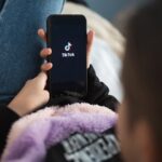 Nizhny Novgorod, Russia - October 03 2020: child with phone in his hands is lying at home on bed. Social Media tiktok is loaded on screen